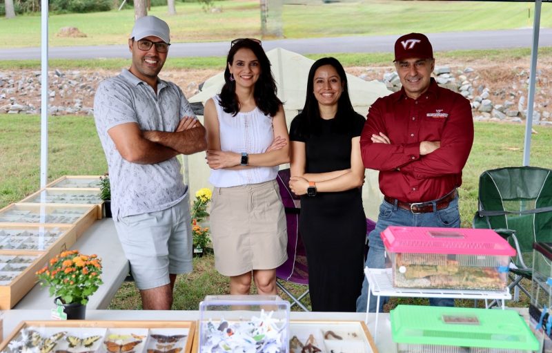 Two women and two men stand behind a table with insect samples during a community field day event.