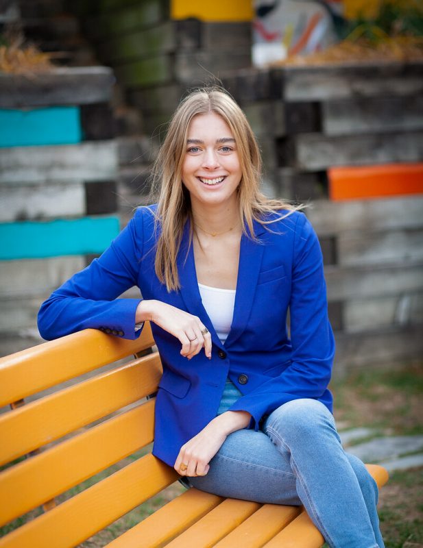 Young woman seated on bench wearing blue jacket.