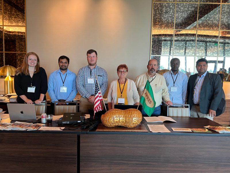 Group of faculty and students standing together behind table at APRES meeting in Oklahoma City, July 2024.