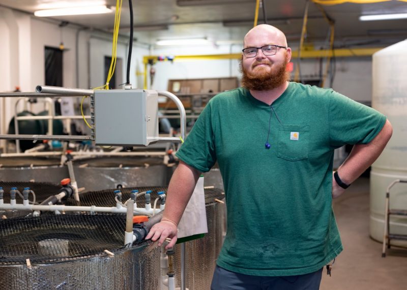 Ethan McAlhaney stands  by recirculating aquaculture system tanks at the Virginia Seafood Agricultural Research and Extension Center.