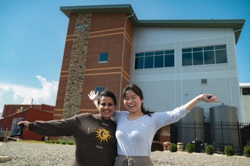 Inayat Batish and Thet Aung raise arms in front of the new Virginia Seafood AREC facility.