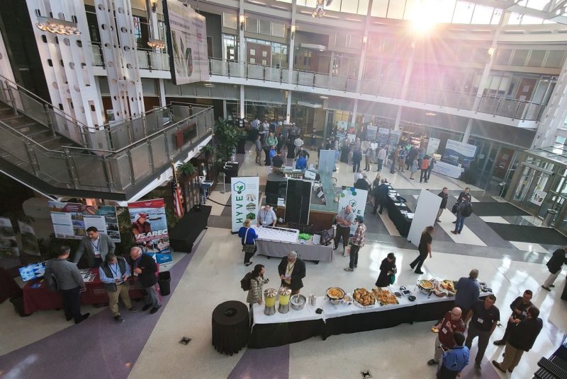 People gathered for a conference around display tables featuring CEA exhibits.