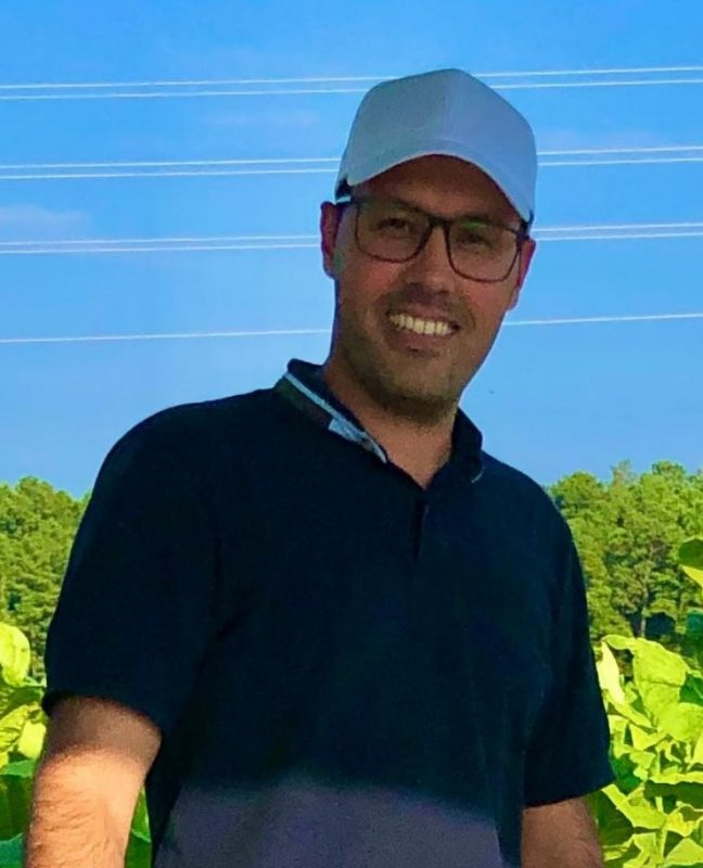 Scientist wearing ball cap and glasses in tobacco field.