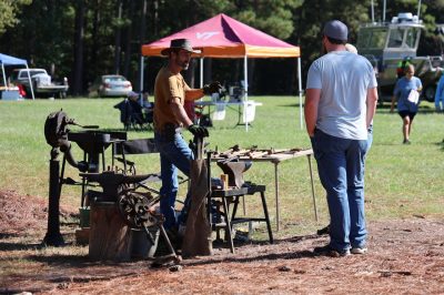 A blacksmith talks with a man looking at his tools
