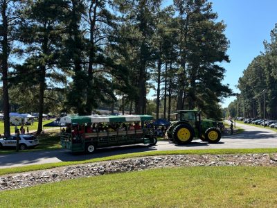 A green tractor pulls a wagon load of people