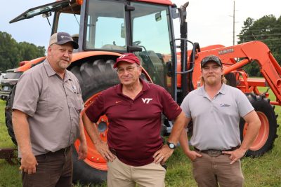 Three men stand in front of an orange tractor