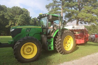 A green tractor pulls a red wagon loaded with people