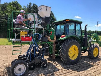 Scientist in field, riding on planter.