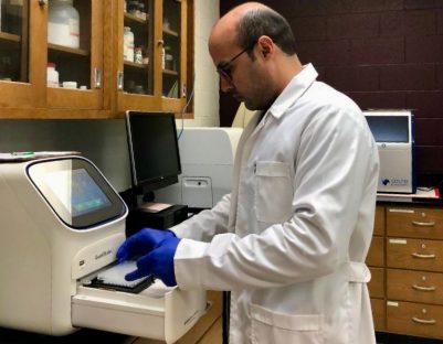 Man in lab wearing coat and gloves.