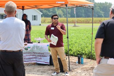 A man in sunglasses speaks to a group of cotton field day attendees.