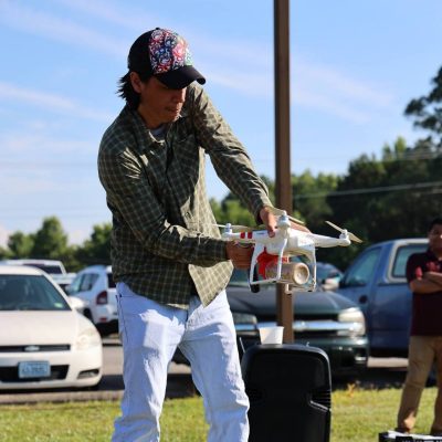 Man in baseball cap and plaid shirt prepares drone for flight in the field at Tidewater AREC.