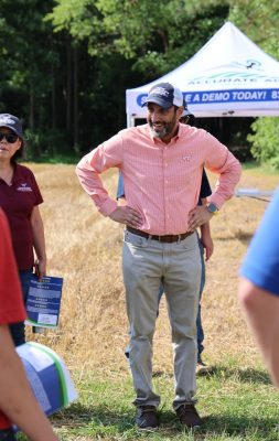A man in a baseball cap interacts with a group of people in the field during the precision ag expo.
