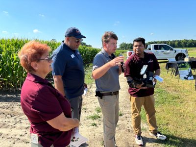 A vendor discusses a hand held device with faculty members in the field during the Precision Ag Expo.