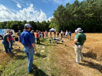 Precision Ag Expo attendees stand around drone in the field prior to a demonstration.