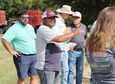 A man in cap gestures and smiles as he speaks to the group at PVQE field day.