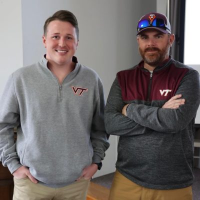 Two men wearing Virginia Tech sweatshirts stand together  in the auditorium at the cover crop field.