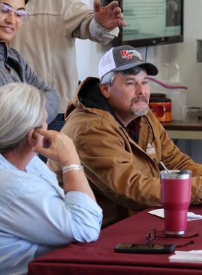 A man wearing a khaki jacket smiles from the registration table during cover crop field day