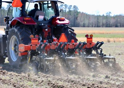A red tractor pulls a soil tillage implement in the field during cover crop field day
