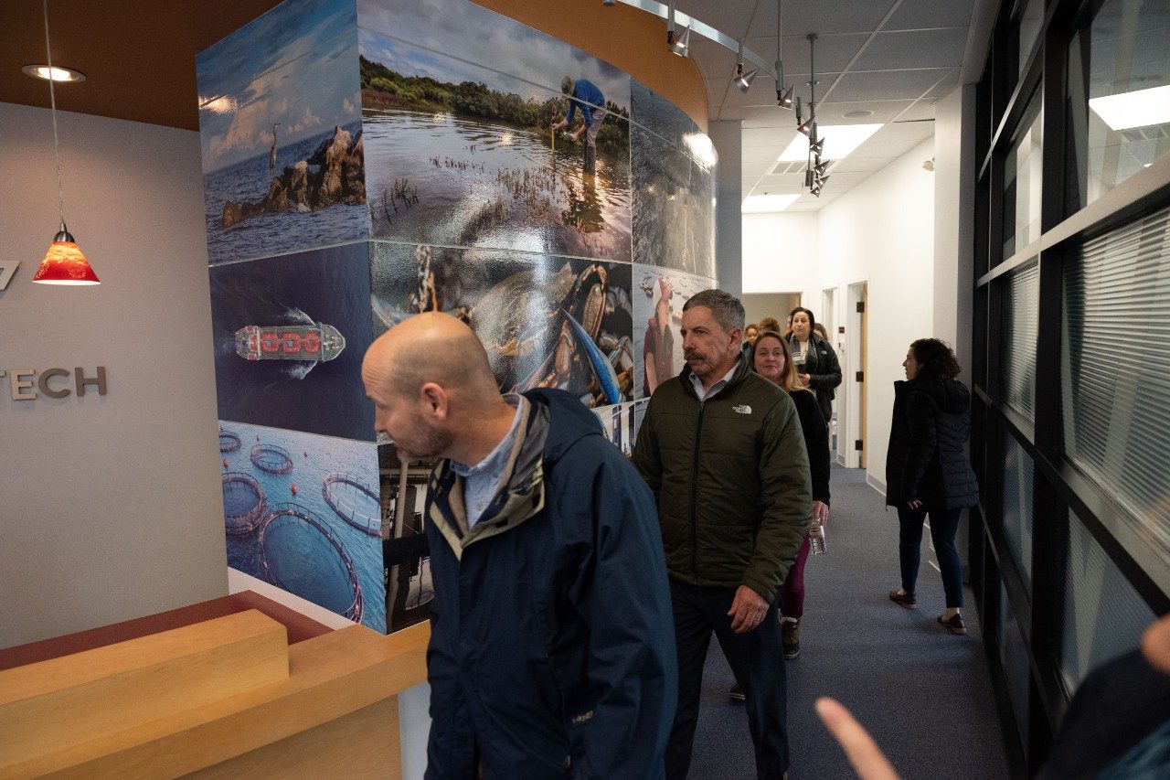 people walking in hallway with pictures of coastal industries  on the walls