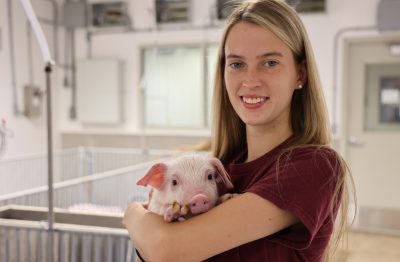 Young woman holds piglet in swine unit.